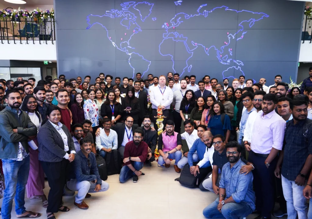 A large group of people posing together indoors in front of a large world map wall