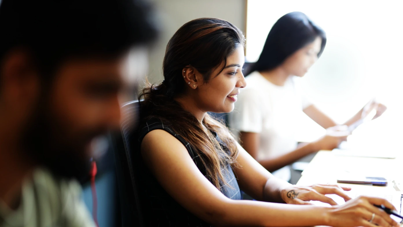 three people sitting at desk working laptop