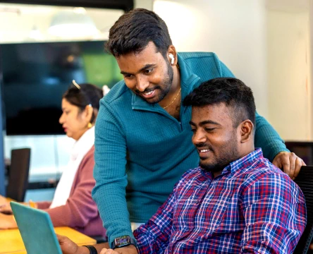Two coworkers collaborating at a desk in an office while looking at a laptop