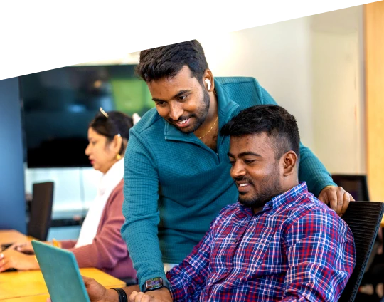 Two coworkers collaborating at a desk in an office while looking at a laptop