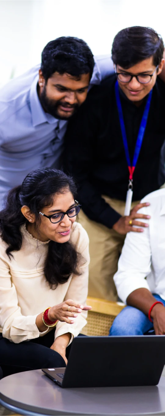 a group of coworkers gathered around laptops, smiling and collaborating in a bright modern office