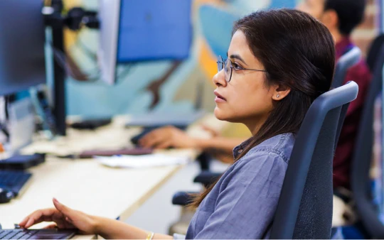 Woman wearing glasses seated at a desk in an office.