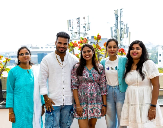 People posing together on a rooftop terrace with flowers and a cityscape in the background.
