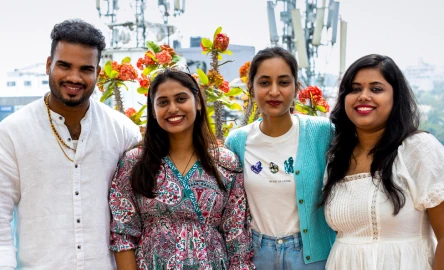 People standing together outdoors, smiling at the camera, with flowers in the background