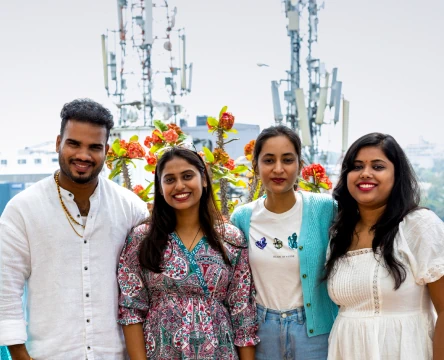 People standing together outdoors, smiling at the camera, with flowers in the background.