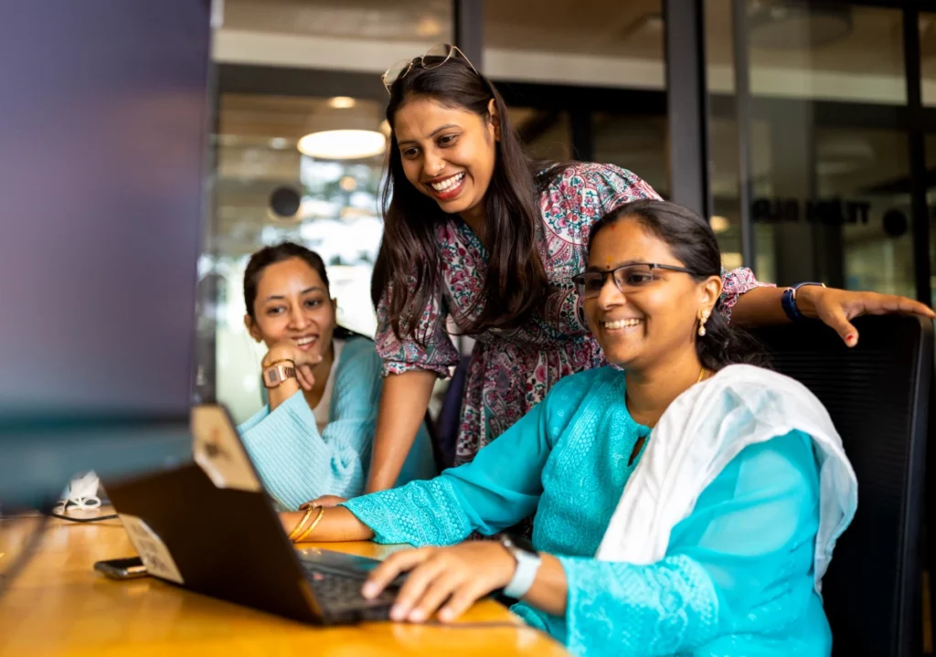 People gathered around a laptop, smiling and collaborating in an office setting.