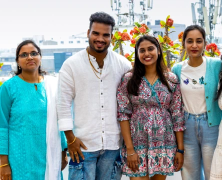 People standing together outdoors, smiling at the camera, with flowers in the background.