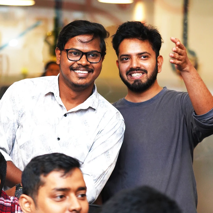 Two smiling men standing together at an indoor team event.