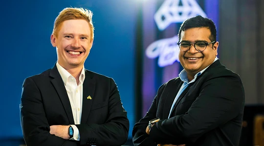 Two men in suits smiling with arms crossed at a corporate event