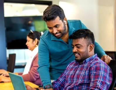 Two coworkers collaborating at a desk in an office while looking at a laptop